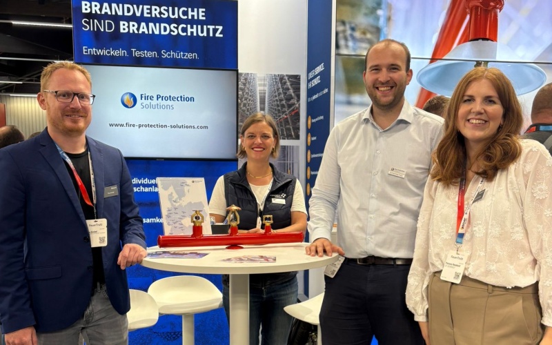 Vier Personen im Gespräch an einem Brandschutz-Messestand mit Infobannern