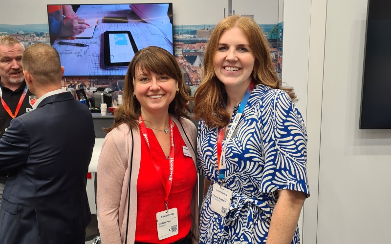 Zwei Frauen am Honeywell-Messestand mit Banner zu vernetzter Gebäudetechnologie