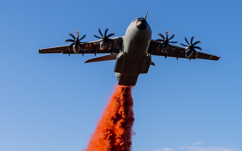 Propellermaschine im Flug lässt leuchtend rot eingefärbtes Löschmittel über einem Feld ab