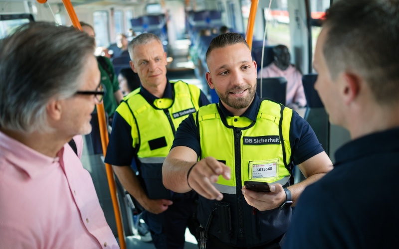 Zwei Männer mit gelben Westen mit Aufschrift DB Sicherheit bei einer Fahrgastkontrolle im Zug