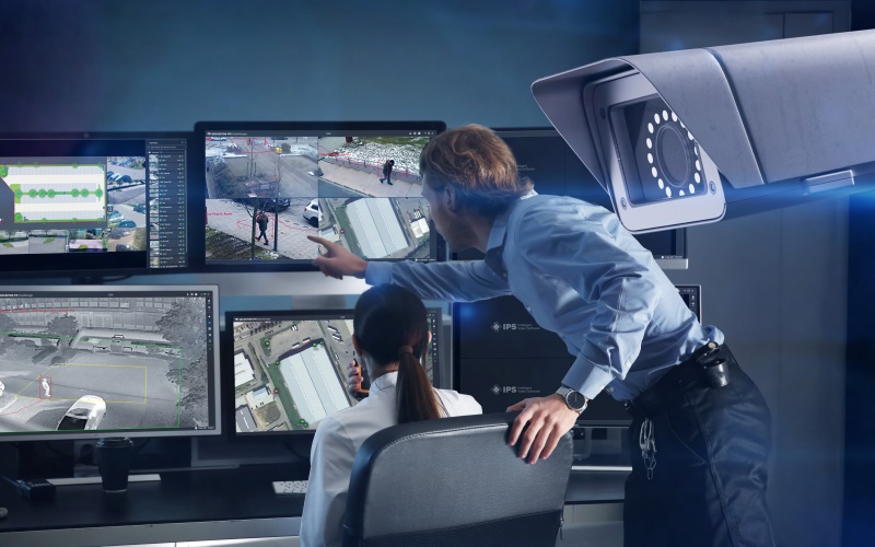 Frau sitzt vor Monitor, davor Mann, der darauf zeigt sowie eine Kamera im Vordergrund