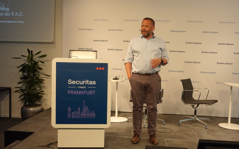 Person steht neben einem Rednerpult mit der Aufschrift „Securitas meets Frankfurt“ in einem Veranstaltungsraum