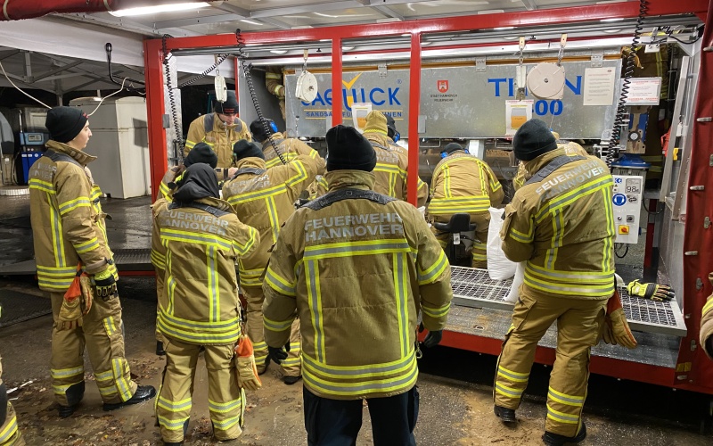 Feuerwehrleute vor beleuchtetem Gestell zur Sandsackbefüllung