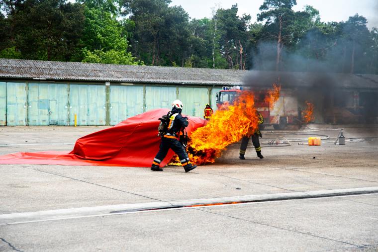 Feuerwehrleute in Schutzkleidung überziehen ein brennendes E-Fahrzeug mit...