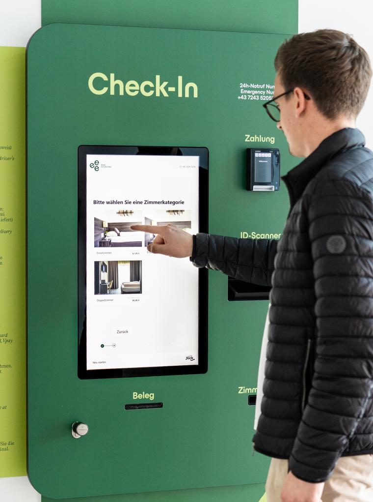 Ein Mann in schwarzer Jacke tippt mit den Finger auf ein großes Display....