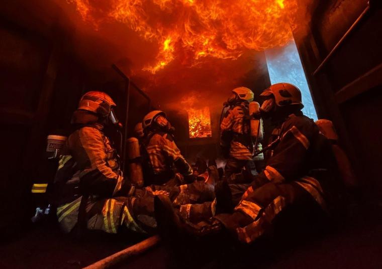 Vier Feuerwehrleute mit Atemschutz und Schutzausrüstung sitzen in einem Raum...