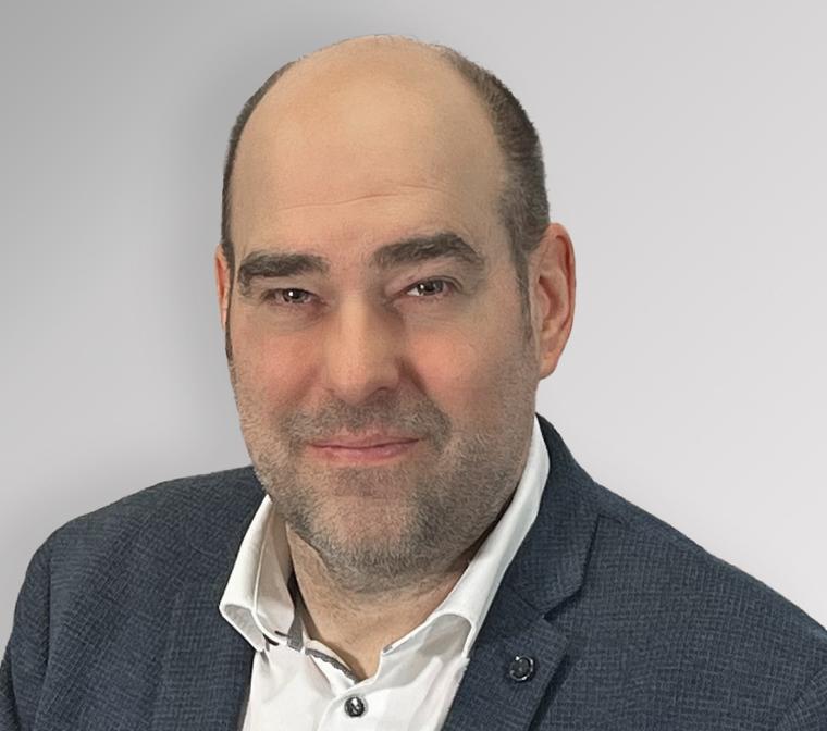 Person in grauem Sakko und weißem Hemd vor einfarbig grauem Hintergrund