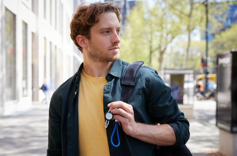 Mann mit gelbem T-Shirt, Jeansjacke, hat auf einer Schulter einen Rucksack mit...