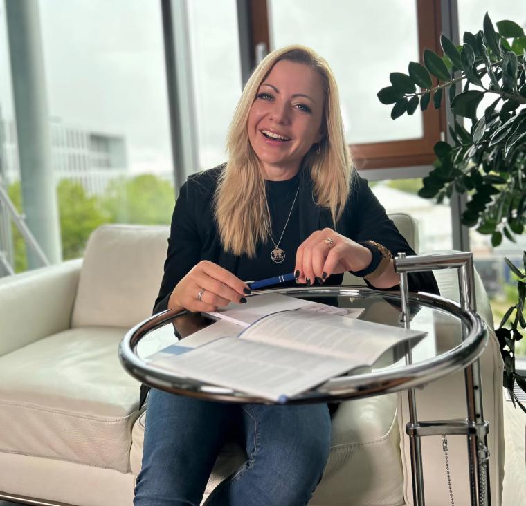 Eine Frau sitzt auf einem weißen Sofa vor einem runden Glastisch. Auf dem...