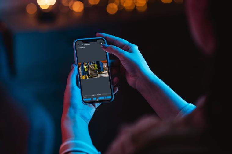 Person hält ein Smartphone, auf dessen Bildschirm eine Überwachungsaufnahme...