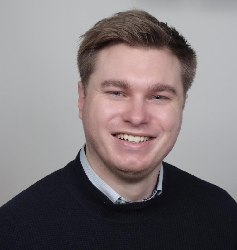 Porträt eines Mannes mit dunkelblauem Pullover über einem hellblauen Hemd vor...