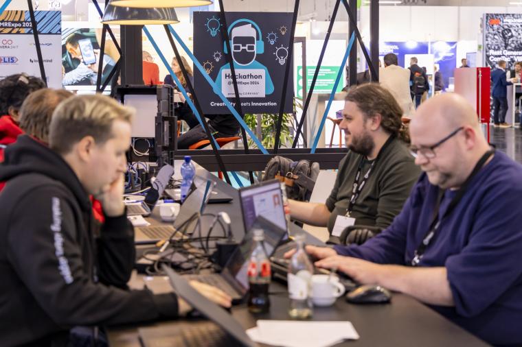 Mehrere Personen, die bei einem Hackathon an Laptops arbeiten. Im Hintergrund...