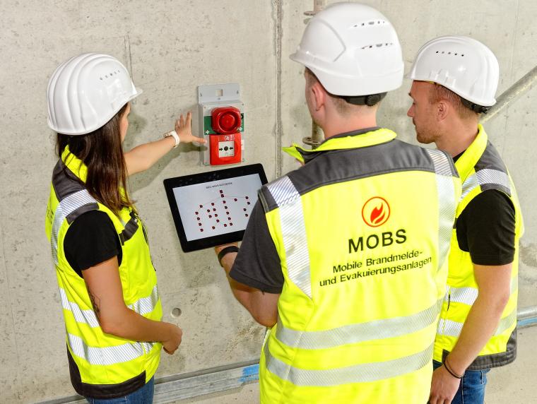Drei Personen mit Tablet vor Alarmierungsgerät