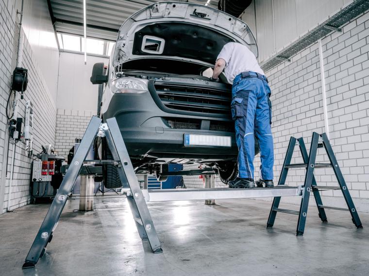 Mechaniker in blauer Arbeitskleidung arbeitet auf Plattform am offenen Motor...