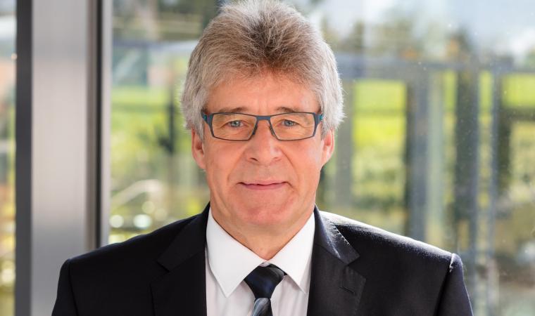 Brustbild einer Person mit Brille, schwarzem Sakko, weißem Hemd, Krawatte