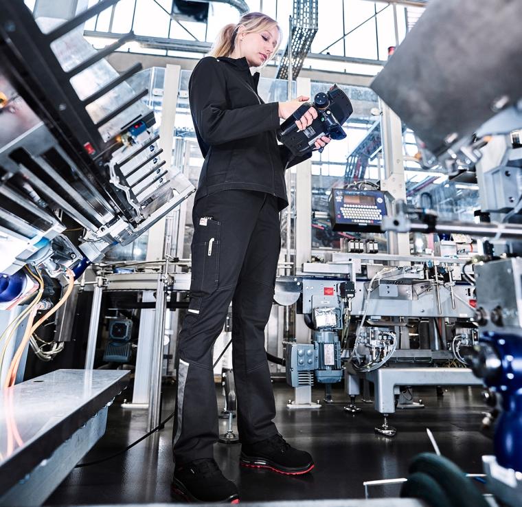 Eine Frau steht in einem modernen, hell beleuchteten Industrieumfeld. Sie...