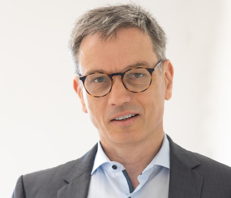 Eine Person mit kurzen grauen Haaren, Brille, hellblauem Hemd und dunkelgrauem...