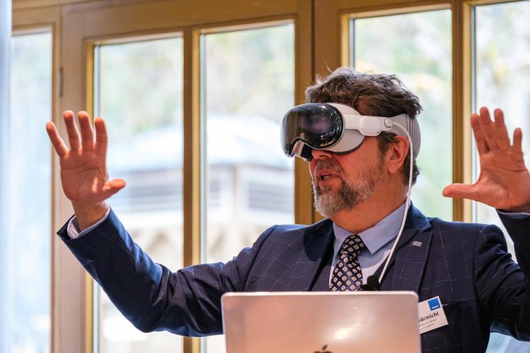 Mann mit Digitalbrille und erhobenen Händen vor aufgeklapptem Rechner