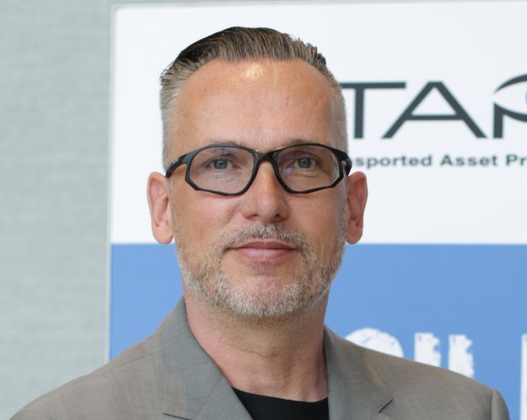 Portrait von Thorsten Neumann mit markanter Brille, hellem Sakko und dunklem...