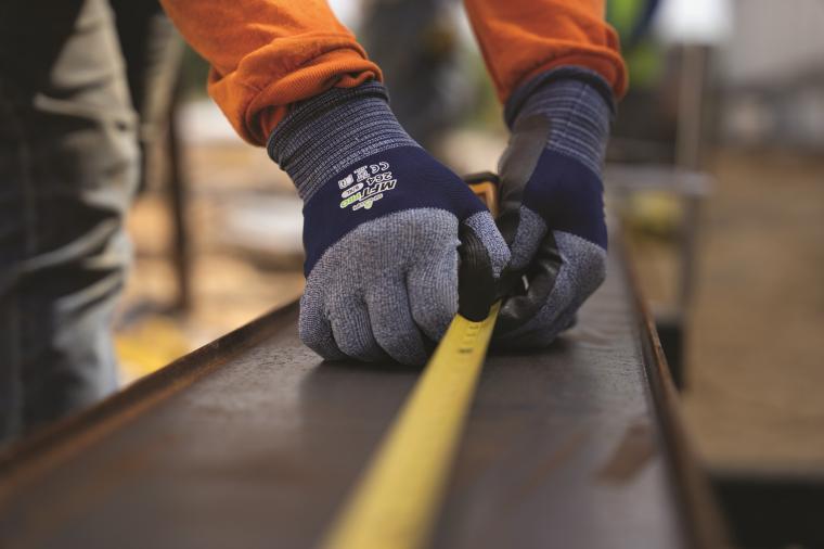 Nahaufnahme von zwei Händen mit Arbeitshandschuhen, die ein Maßband an einem...