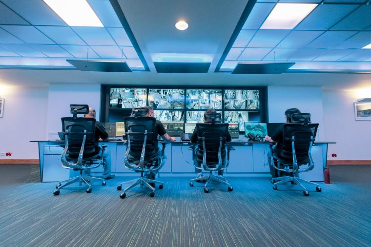 Rückansicht von vier Mitarbeitern, die vor einer Monitorwand arbeiten