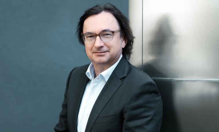 Portrait eines mittelalten Mannes mit Sakko vor einer grauen Wand