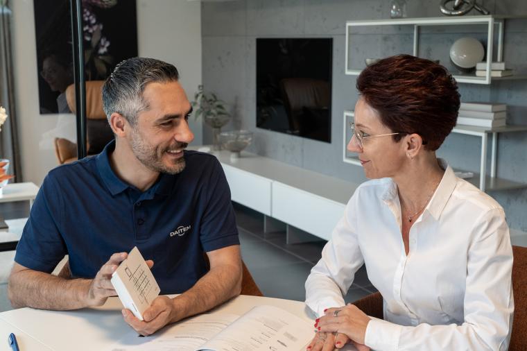 Mann und Frau am Tisch sitzend. Der Mann zeigt ihr eine kleine weiße...