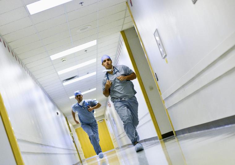 Zwei Ärzte in blauen Arztanzügen und Mützen rennen durch einen...