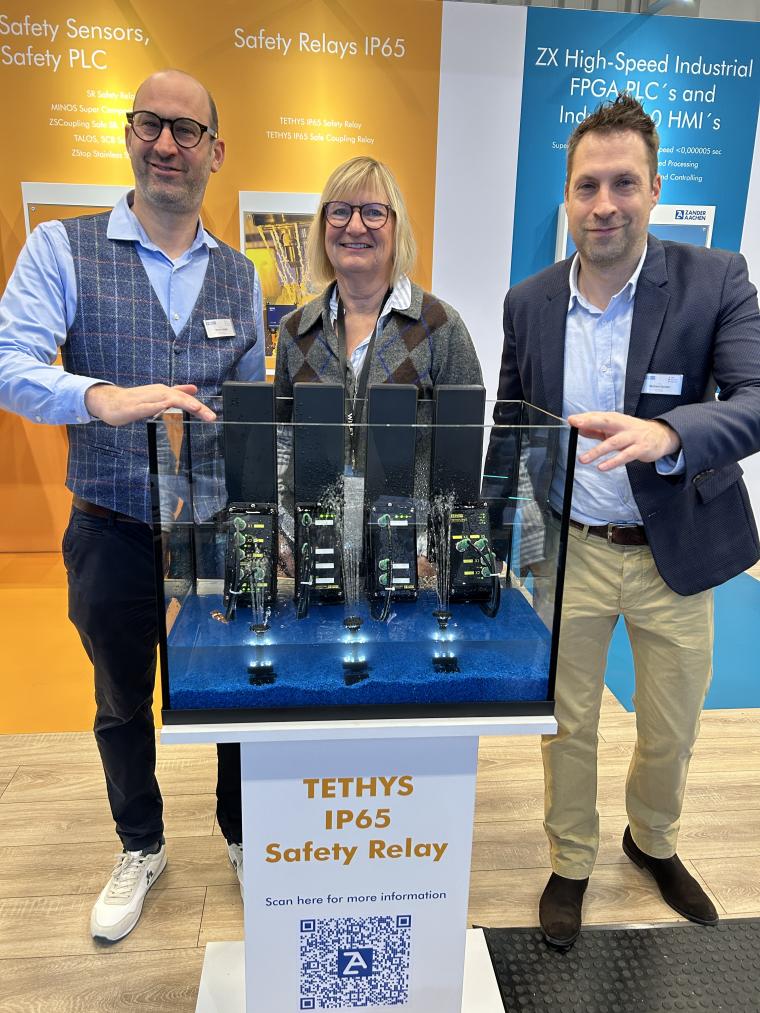 zwei Männer, eine Frau auf einer Messe vor einem Exponat