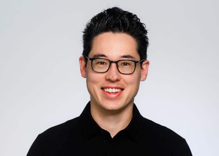 Eine Person mit dunklen, kurzen Haaren trägt ein schwarzes Poloshirt vor...