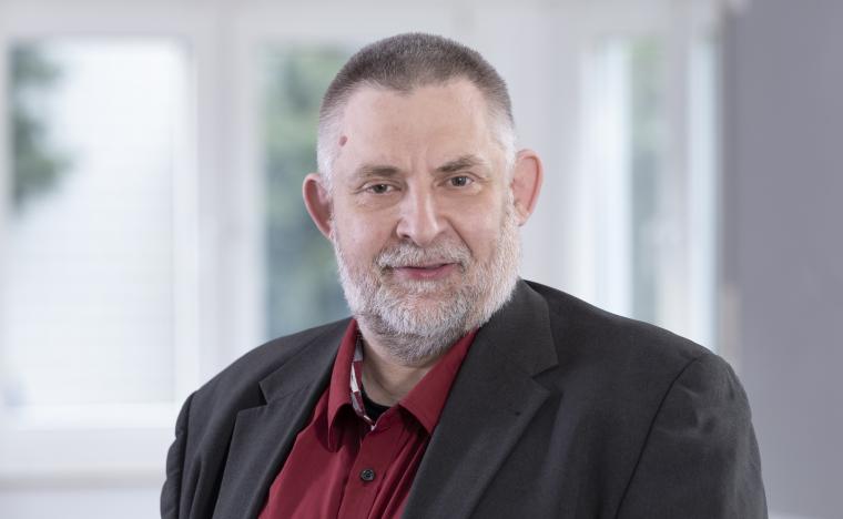 Älterer Herr mit grauem Bart, schwarzem Sakko und rotem Hemd