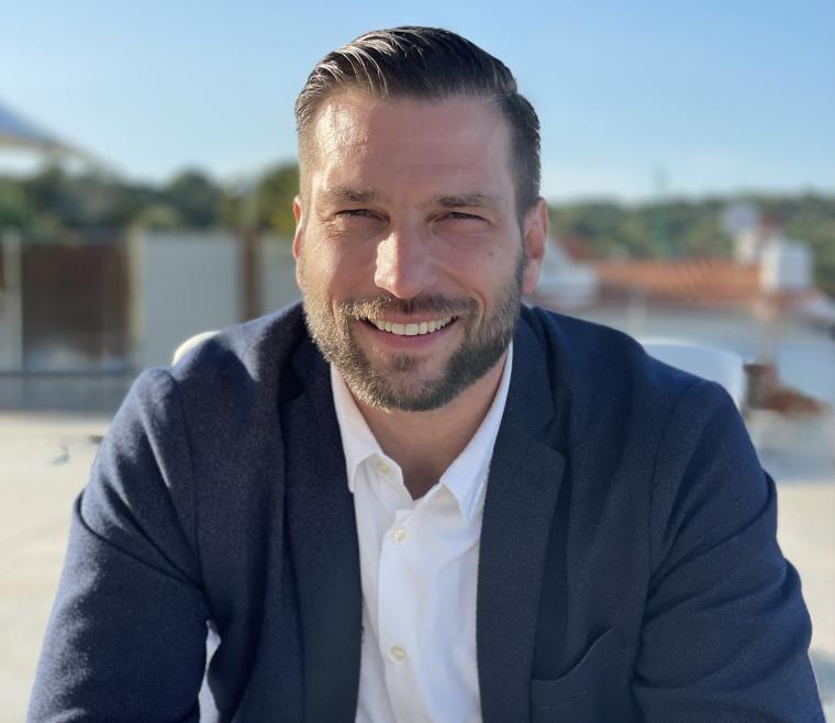 Smiling, seated younger man with blue jacket and white shirt