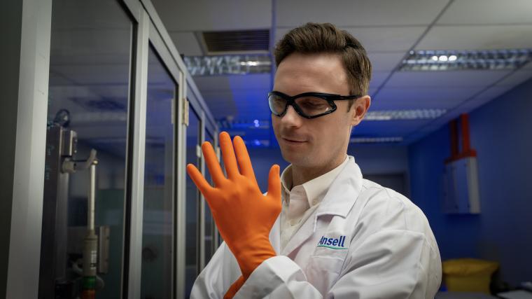 Person im Labor trägt einen weißen Laborkittel und orangefarbene...