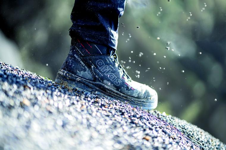 Ein staubiger Sicherheitsschuh steht auf einer grobkörnigen, steilen...