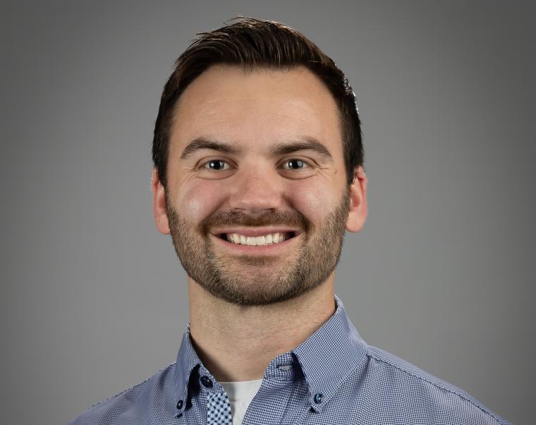 Portrait von Connor Doherty, lächelnd mit dunklem Haar und Bart. Er trägt ein...