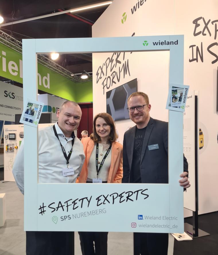 Drei Personen stehen an einem Messestand von Wieland Electric und posieren...