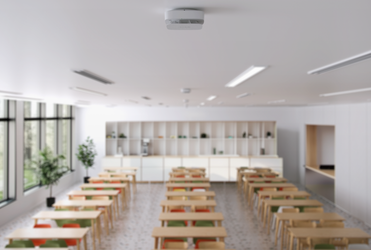 Rauch- oder Brandsensor an der Decke eines hellen Klassenzimmers mit geordneten...