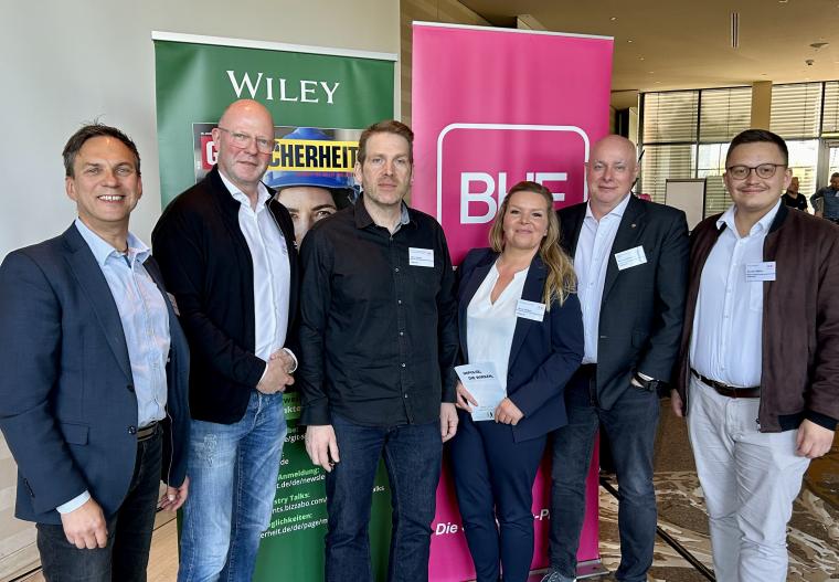 Fünf Männer und eine Frau stehen vor zwei Bannern