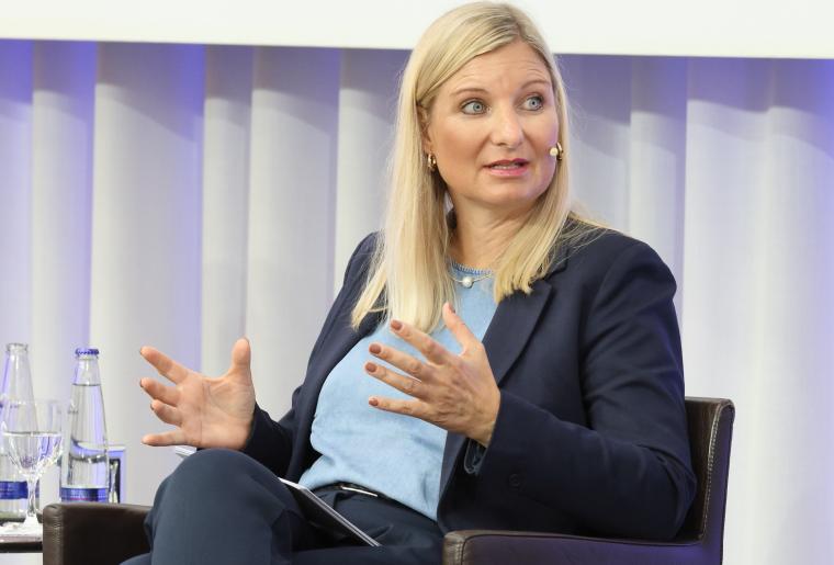 Frau mit längeren blonden Haaren auf einem Sessel sitzend mit erläuternder...