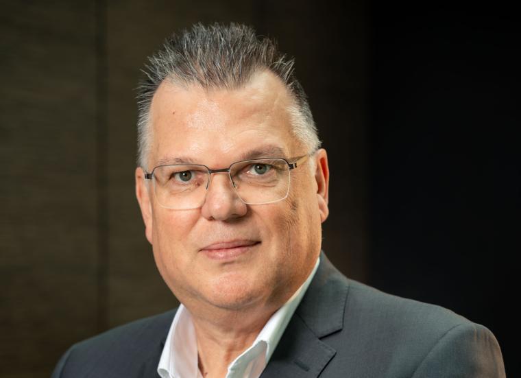 Porträtaufnahme einer Person im dunklen Sakko und hellen Hemd vor neutralem,...