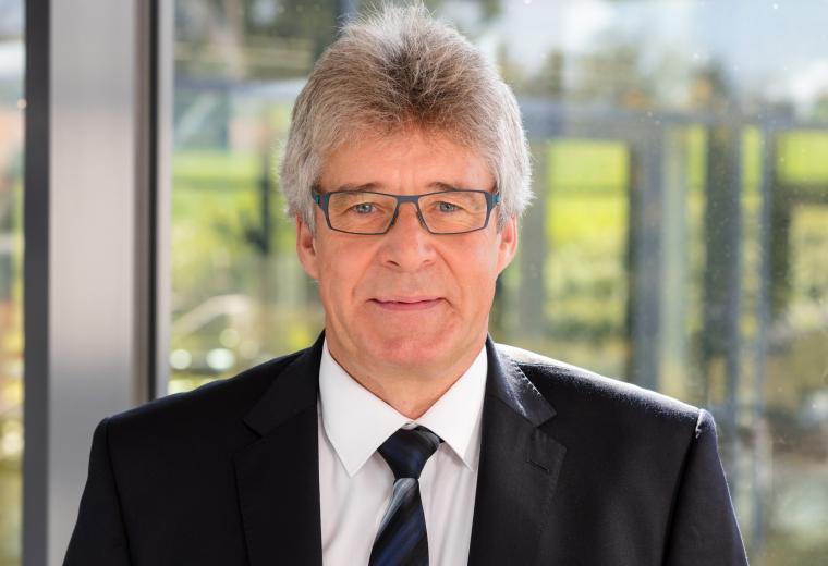 Mann mit grauen Haaren, Brille, Anzug und gestreifter Krawatte