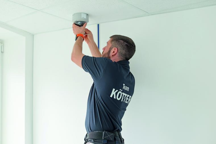 Handwerker, der einen Brandmelder an einer Zimmerdecke befestigt