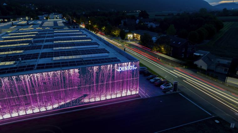 Luftaufnahme eines Firmengebäudes bei Nacht mit beleuchteter Fassade,...