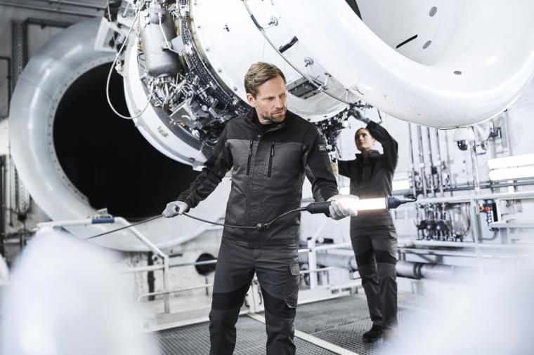 Zwei Personen in Schutzkleidung arbeiten in einer Industrieanlage an einer...