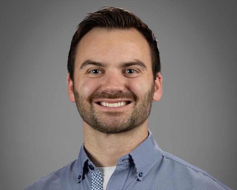 Portrait photo of a person wearing a blue patterned shirt against a gray...