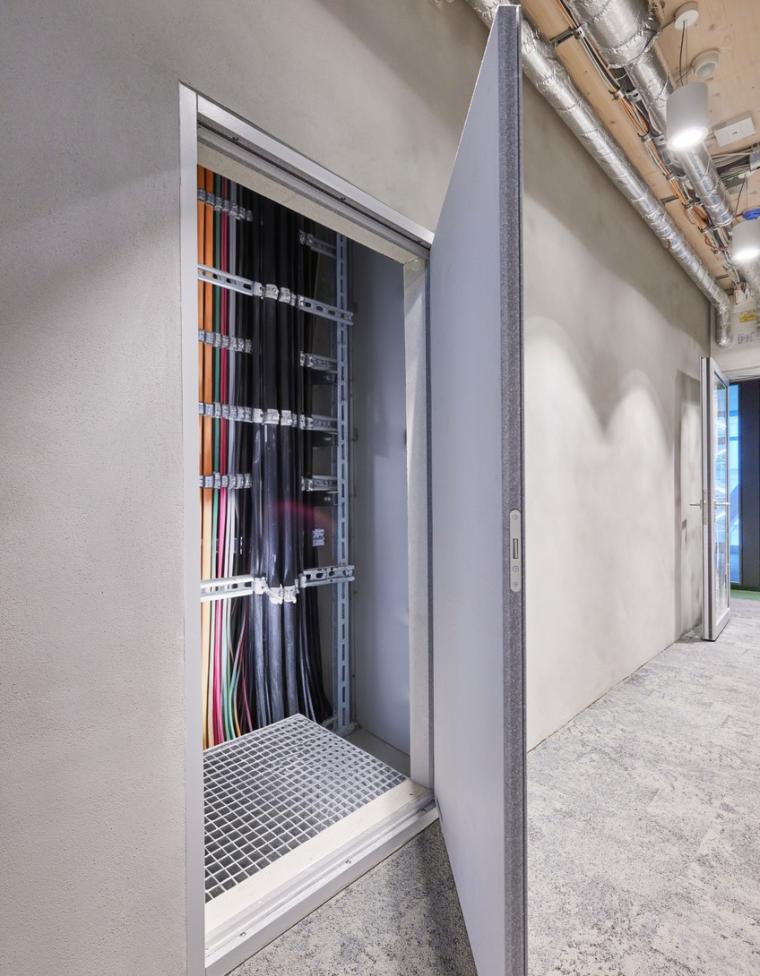 Open fire-rated door in a corridor, revealing a cable riser with bundled cables...