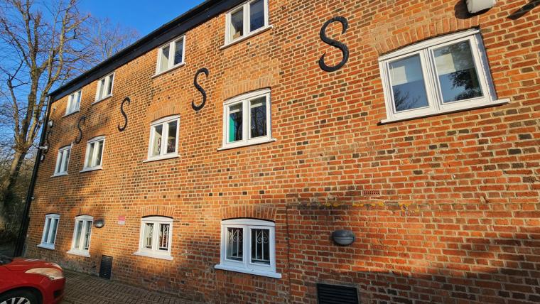 Brick building façade with several white-framed windows and large black letter...