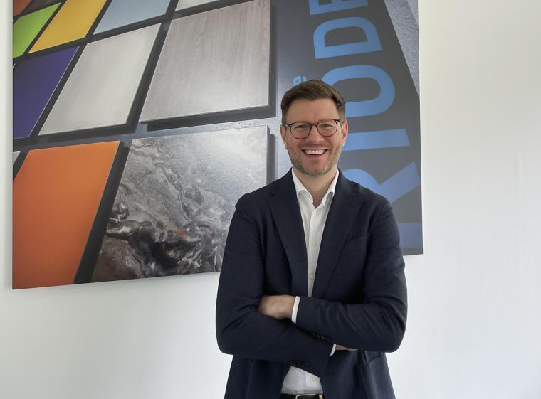 Person in Businesskleidung mit verschränkten Armen steht vor einer Wand mit...