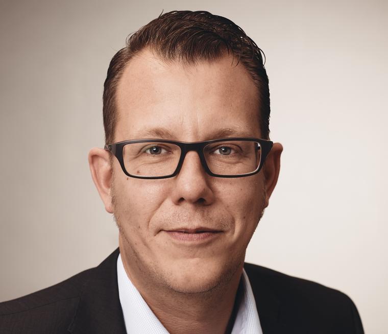 Porträt eines Mannes mit kurzer dunkler Frisur und Brille, der in die Kamera...