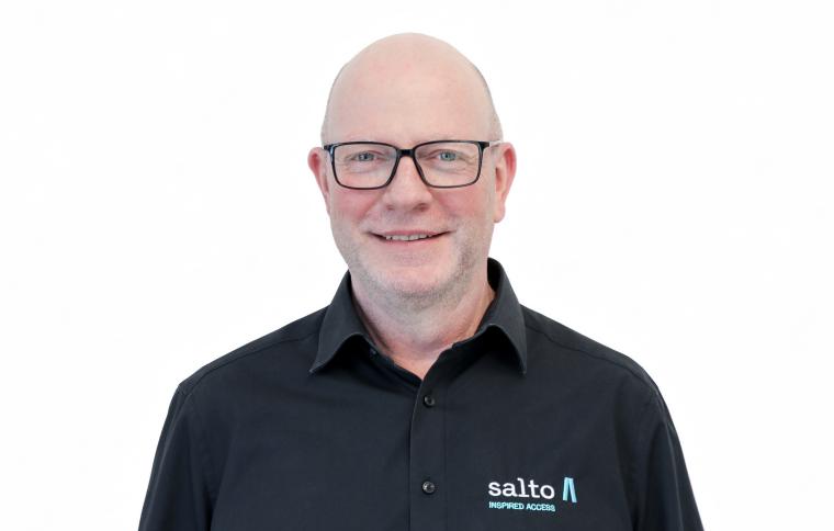 Porträtfoto einer Person mit Brille in schwarzem Hemd mit „SALTO Inspired...